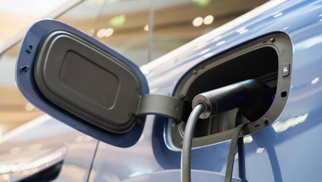 Close-up of a charging port on a blue electric vehicle with a charging cable connected