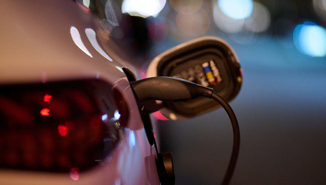 Electric vehicle charging port with cable connected at night, city lights in the background