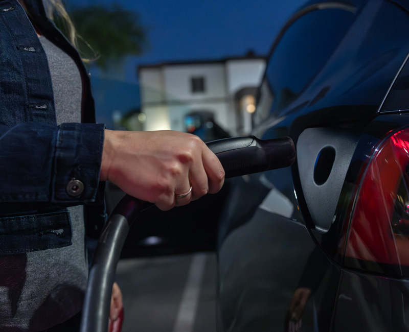 Woman plugging a charging cable into an electric vehicle at night in a residential area