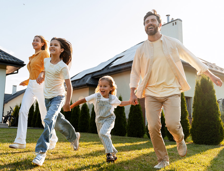 Happy family enjoying their backyard with a home featuring rooftop solar panels in the background.