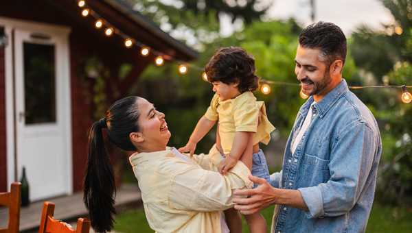 A happy family enjoying the outdoors in their backyard in the evening with string lights glowing behind them.