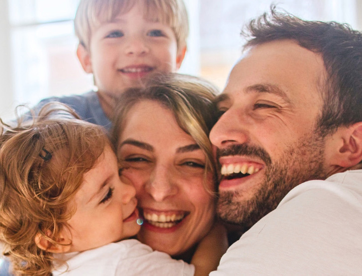 Family cuddling together, with a smiling child hugging an adult in a close-up photo.