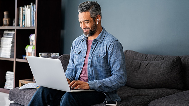 Man using a laptop and earbuds on a living room couch